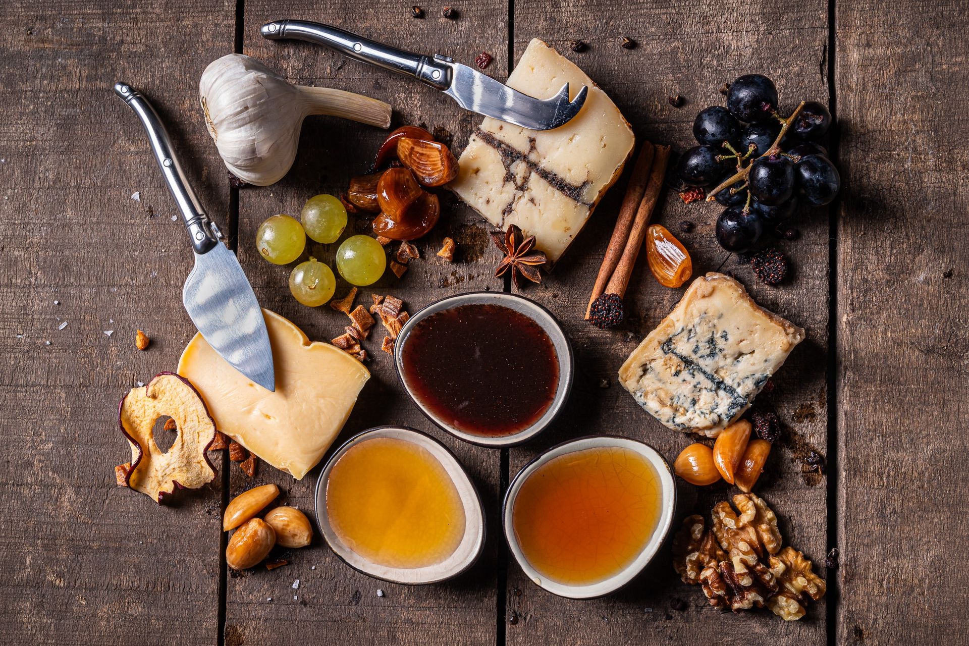 Kaasplank van bovenaf met drie schaaltjes honingsap, fruit en knoflook